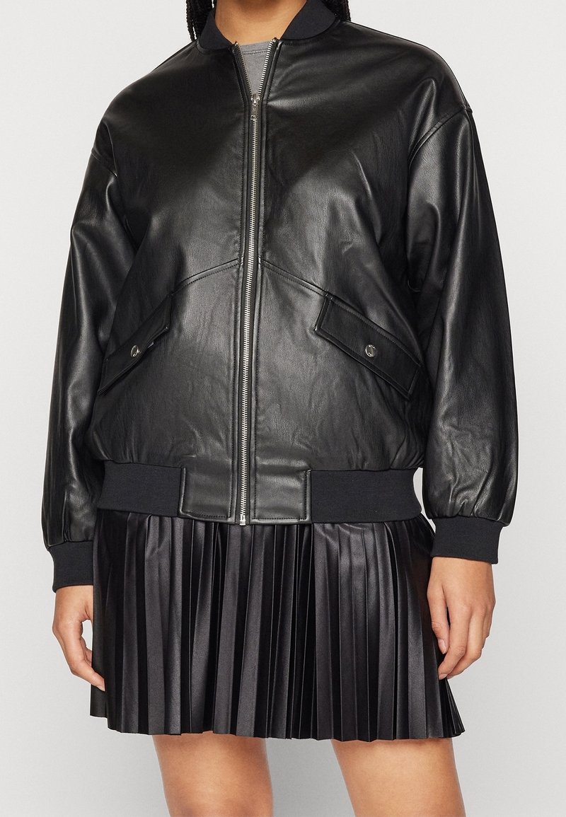 Svart läderbomberjacka med dragkedja fram, ribbade ärmslut och två sidofickor. Har en slät textur och en strukturerad passform. Plisserad svart kjol.