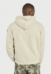 Beige hoodie med snøre i hætten, oversized pasform og blød tekstur. I kombination med bukser i camouflage-mønster for ekstra detaljer.