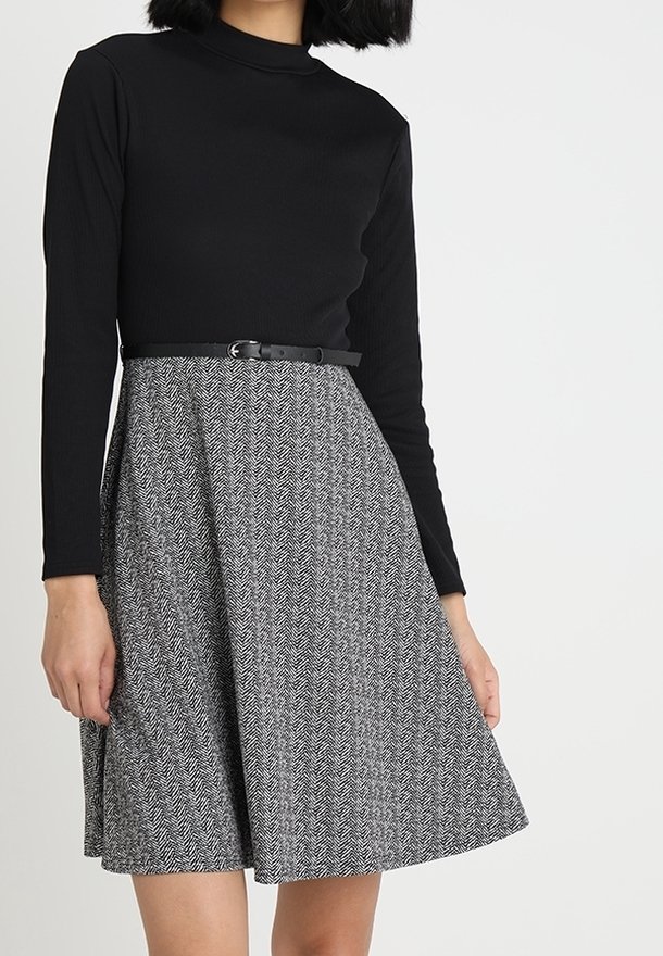Svart långärmad topp kombinerad med en knälång kjol med hundtandsmönster i svart och vitt, accentuerad med ett smalt svart skärp.