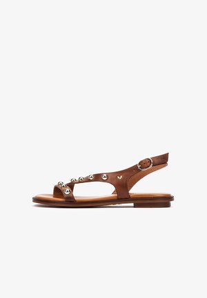 Brown leather sandals with a flat sole, open toe, and a T-strap design, featuring silver round studs and an adjustable ankle buckle.