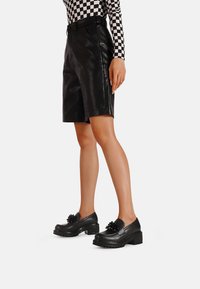 Pantaloni corti neri in pelle con una texture liscia e elegante. Abbinati a scarpe nere con un accento floreale e una suola spessa e robusta.