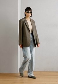 Blazer oversize verde oliva, top beige, vaqueros baggy azul claro, zapatos grises de tipo slip-on y gafas de sol oscuras. Texturas suaves, corte casual.