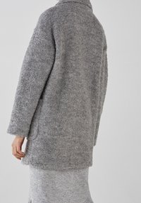 Grå, fluffig overcoat med krage, långa ärmar och sidofickor. Mjuk textur och avslappnad passform, visad från baksidan.