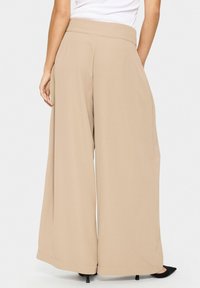 Pantaloni beige a gamba larga con vita alta, realizzati in un tessuto liscio. Presentano tasche laterali e una vestibilità rilassata, orlati in fondo.