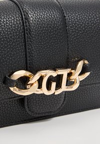 Borsa a mano in pelle nera testurizzata con una catena d'oro prominente con le lettere "G" e "Z" come dettaglio della chiusura.