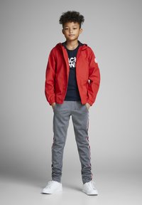 Rdeča lahka jakna s kapuco, mornarsko modra majica, sivi trenirki z rdečimi in belimi stranskimi črtami ter bele teniske.