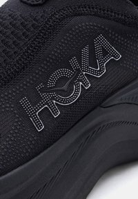 Κοντινό πλάνο υφάσματος μαύρου αθλητικού παπουτσιού με υφή στη σόλα και ανάγλυφο λογότυπο με τελείες ενσωματωμένο στο πλαϊνό πάνελ.