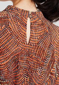 Korte mouwen blouse met een gekleurde abstracte print in oranje, zwart en wit, met een sleutelgat aan de achterzijde en een sluiting met twee knopen.