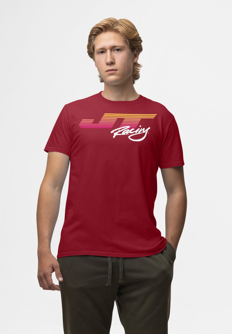 Röd bomull t-shirt med en flerfärgad grafik av "JT Racing" med horisontella linjer i rosa och orange, korta ärmar och rund hals.