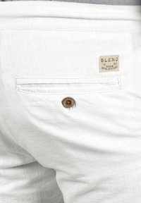 Shorts en lin blancs avec une poche arrière ornée d'un bouton en bois et d'une étiquette de marque indiquant "BLEND 1993 DENIM WITH ATTITUDE".