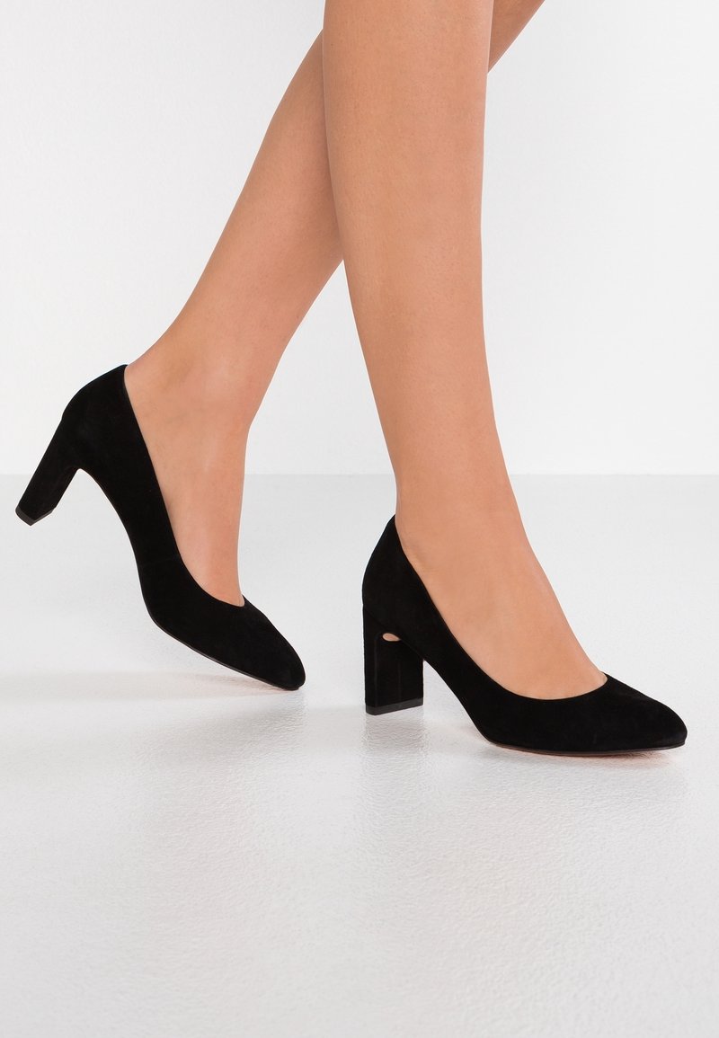 Pumps neri in suede con tacco alto, punta arrotondata e tacco a blocco. La parte superiore ha una texture liscia e un design a scollo basso.