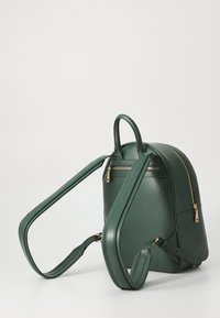 Grüner Kunstleder-Rucksack mit glatter Textur, runder Form, verstellbaren Trägern und einer Fronttasche mit Reißverschluss und goldenen Beschlägen.
