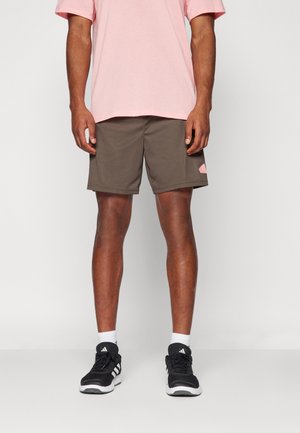 Herroutfit bestående av en rosa t-shirt i bomull och bruna atletiska shorts med en sidopatch. Bärs med svarta atletiska skor och vita strumpor.