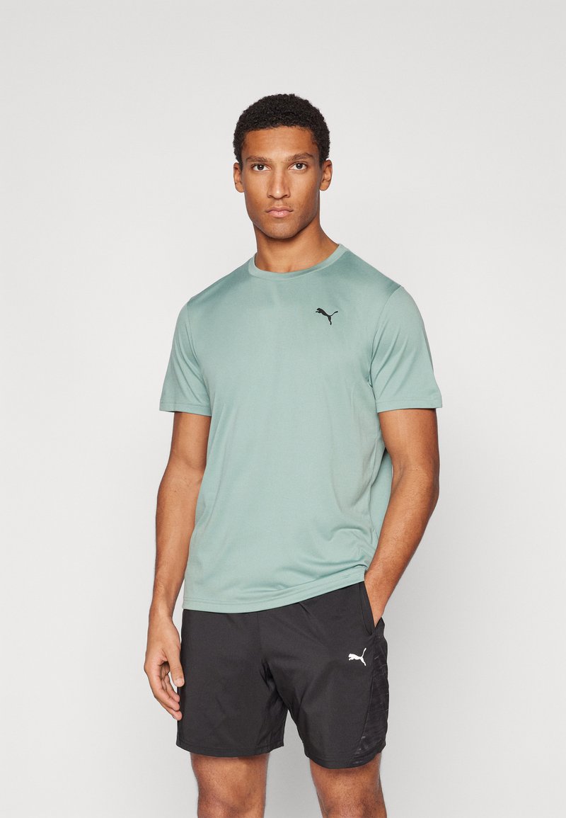 Camiseta deportiva de color verde claro con un logo de Puma negro; de manga corta y cuello redondo, combinada con pantalones cortos negros.