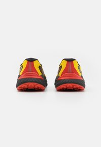 Scarpe da trail running nere e rosse con dettagli gialli. Presentano una tomaia in rete testurizzata, una suola robusta e un battistrada pronunciato per la trazione.