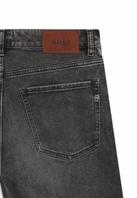 Jeans in denim nero con una patch in pelle BOSS sulla vita, caratterizzati da cuciture bianche a contrasto e una sola tasca posteriore con dettagli del logo.