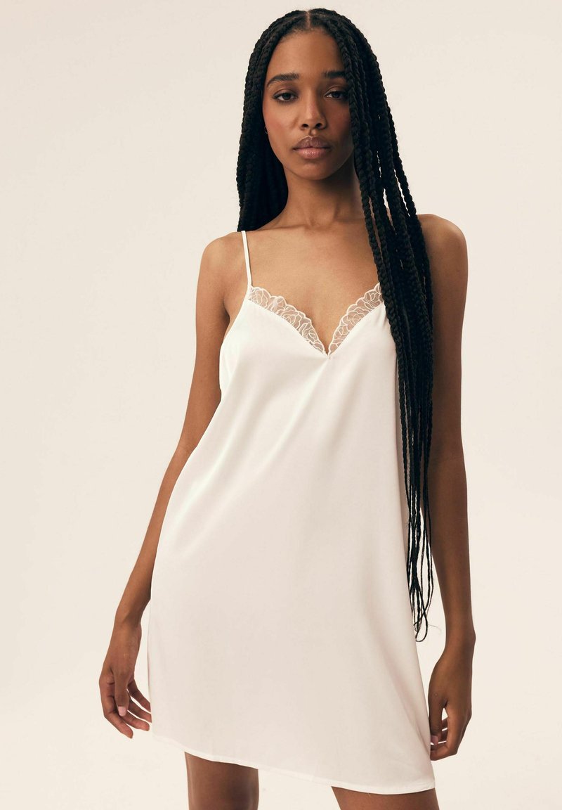 Biała satynowa sukienka na ramiączkach z koronkowym wykończeniem dekoltu i regulowanymi ramiączkami. Gładka tekstura, długość do kolan.