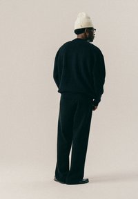 Black oversized sweater with dropped shoulders, paired with loose black pants. Accessories include a cream knit beanie and round glasses.