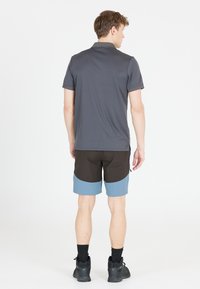 Kortärmad grå polo tröja, tillsammans med svarta och ljusblå shorts. Avslappnat fot, med en texturerad yta, visad bakifrån.