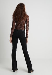 Top z motywem panterki z długim rękawem, zestawiony z dopasowanymi czarnymi spodniami dzwonami o średnim stanie i subtelnymi detalami przeszycia.