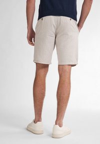 Pantaloni corti a righe beige realizzati in morbido tessuto, con orlo arrotolato, due bottoni posteriori e una vestibilità a vita media. Abbinati a sneakers bianche.