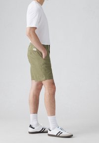 Shortsit oliivinvihreä, kevyestä kankaasta valmistettu, jossa on sivutaskut ja takatasku. Yhdistetty yksinkertaisen valkoisen t-paidan ja valkoisten lenkkarien kanssa.