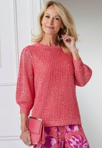 Rosa gestrickter Pullover mit einem lockeren, strukturierten Design und puffärmel, kombiniert mit einer rosa Clutch und Hose mit floralem Muster.