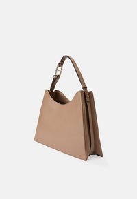 Sac à main en cuir beige avec une forme structurée et un haut arrondi. Comprend une bandoulière amovible en cuir marron avec des ferrures couleur or.