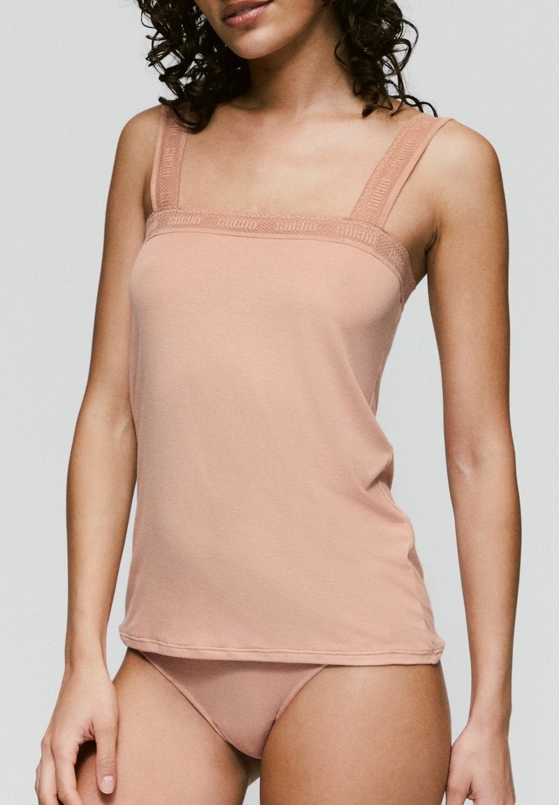 Lichtroze cami-top met verstelbare bandjes en een gegolfde kantafwerking. Zachte, rekbare stof met een aangesloten pasvorm en een afgeronde zoom.
