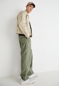 Beige jacket, olive green cargo pants, and white sneakers. The jacket has button details; the pants feature side pockets and a loose fit.