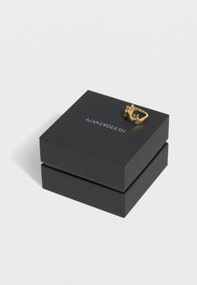 Μαύρο κλειστό κουτί κοσμημάτων με λευκό λογότυπο "NANEROTETTI" και ένα χρυσό δαχτυλίδι σε αφηρημένο σχήμα που ακουμπά στο καπάκι.
