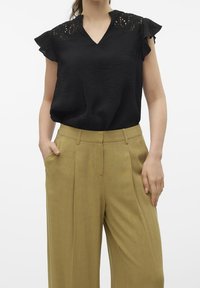 Czarna bluzka z koronkowymi detalami na ramionach, dekoltem w serek i krótkimi falbaniastymi rękawami, zestawiona z wysokim stanem, szerokimi spodniami w jasnym oliwkowym odcieniu.