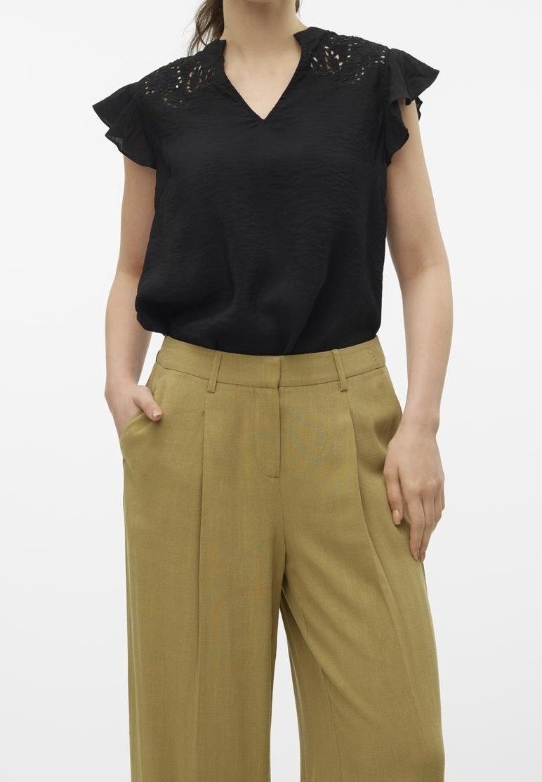 Czarna bluzka z koronkowymi detalami na ramionach, dekoltem w serek i krótkimi falbaniastymi rękawami, zestawiona z wysokim stanem, szerokimi spodniami w jasnym oliwkowym odcieniu.