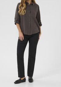 Chemise grise à boutons avec manches longues retroussées aux poignets, associée à un pantalon droit noir et des mocassins noirs.