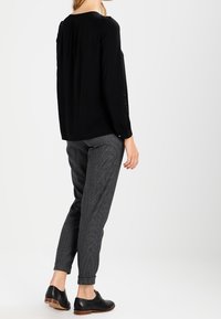 Maglietta nera a maniche lunghe con vestibilità rilassata e scollatura rotonda, abbinata a pantaloni grigi texturizzati, con orlo risvoltato alla caviglia, e scarpe eleganti nere.