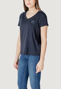 T-shirt in cotone blu navy con scollo a V e una piccola patch con logo sul lato sinistro del petto. Maniche corte, vestibilità comoda, texture liscia.