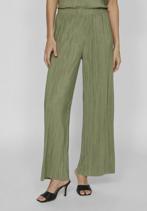 Groene geplooide wijde broek met een gestructureerde afwerking, voorzien van een elastische tailleband en gedragen met zwarte hoge open teen muilen.