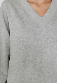 Sudadera gris de cuello en V con una textura suave y un corte relajado, con un diseño simple y sin patrones ni acentos visibles.
