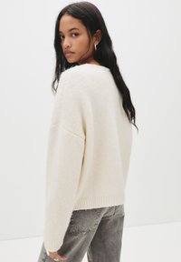 Sweter w kolorze kremowym, dzianinowy, o luźnym kroju, z prążkowanymi mankietami i dołem, w połączeniu z szarymi dżinsami; miękka tekstura i swobodny design.