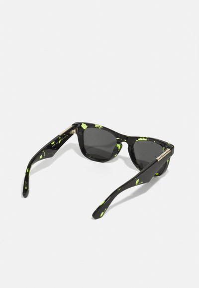 Ochelari de soare negri cu un model punctat neon verde, formă unghiulară, lentile întunecate și brațele elegante, texturate, cu accente subtile de aur.