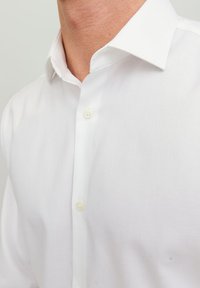 Uomo che indossa una camicia da uomo bianca e impeccabile con colletto classico e due bottoni visibili chiusi sul davanti.