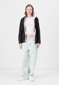 Casaquinho leve preto, top curto rosa pálido e jeans oversized azul claro com um padrão texturizado. Ténis brancos completam o look.