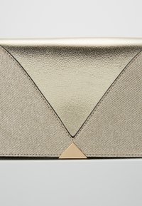 Złota metaliczna kopertówka z teksturowaną powierzchnią, trójkątnym akcentem u podstawy oraz kontrastującą, g�ładką górną częścią.