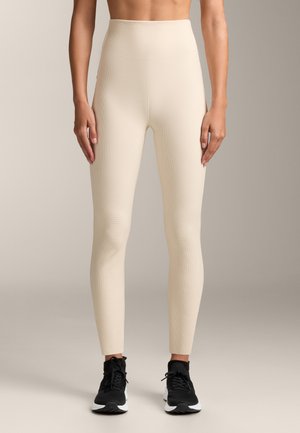 Hoge beige leggings met een structuurpatroon, slim fit ontwerp en gladde stof. Gecombineerd met zwarte sportschoenen.