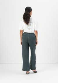 Hvit t-skjorte med grafisk hjerte-design, kombinert med høytlivede, vide mørkeblå jeans og grå høyhælte sko.