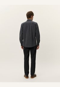 Cămașă cu mânecă lungă de culoare gri închis cu dungi verticale. Prezintă un guler clasic, manșete cu nasturi și un tiv drept. Asortată cu pantaloni negri.