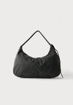 Sac d’épaule en tissu noir doux avec une bandoulière simple et une texture légèrement froissée sur un fond clair uni.