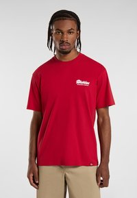 Camiseta de algodón roja con mangas cortas, que presenta un logo blanco en el lado izquierdo del pecho. Dobladillo recto y corte relajado.