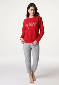 Felpa rossa con design "CLUB Santa" e accenti colorati, abbinata a pantaloni jogger grigi a gamba affusolata realizzati in tessuto morbido.