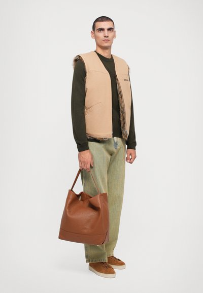 Vesta bej cu trim din blană artificială, cămașă verde cu mâneci lungi, pantaloni verde deschis și geantă de umăr maro din piele, cu o suprafață moale și texturată.